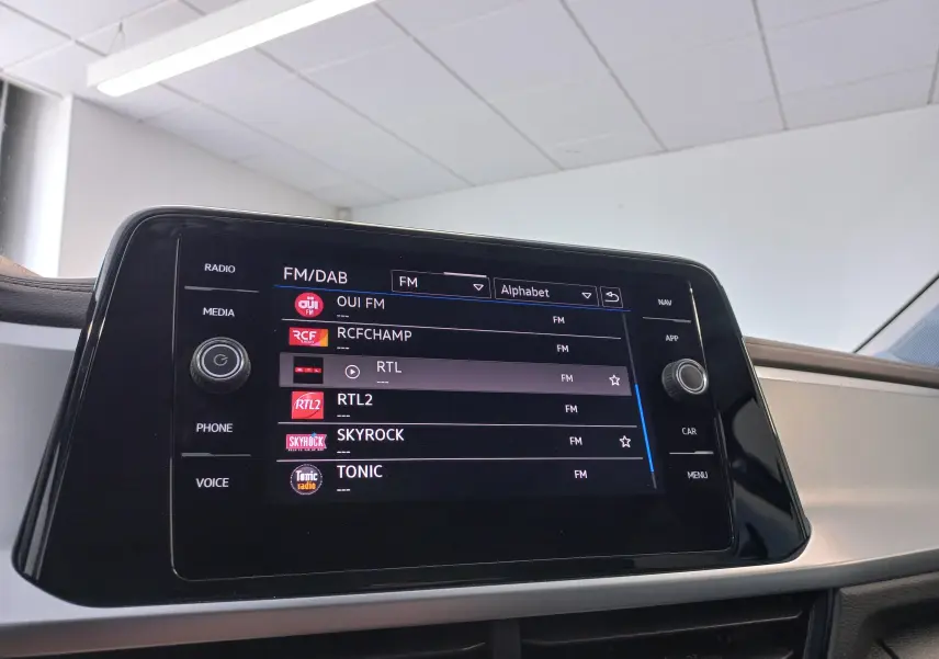 Écran tactile central du Volkswagen T-Roc 2025 affichant les stations radio FM dans un intérieur clair.