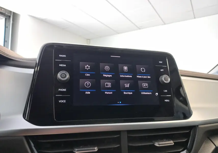 Écran tactile central du Volkswagen T-Roc 2025 affichant le menu principal avec commandes physiques sur les côtés.