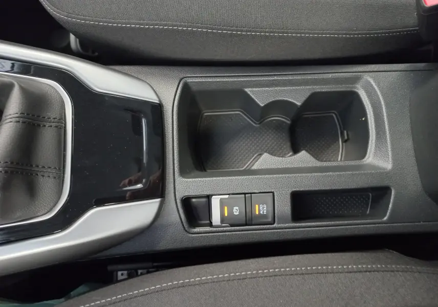 Vue rapprochée de la console centrale du Volkswagen T-Roc 2025, montrant le porte-gobelets et les commandes de frein à main électrique.