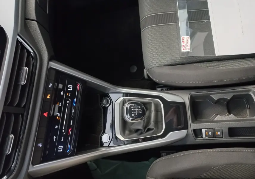 Vue intérieure centrée sur la console centrale du Volkswagen T-Roc 2025, mettant en valeur le levier de vitesse manuel et les commandes climatisation.