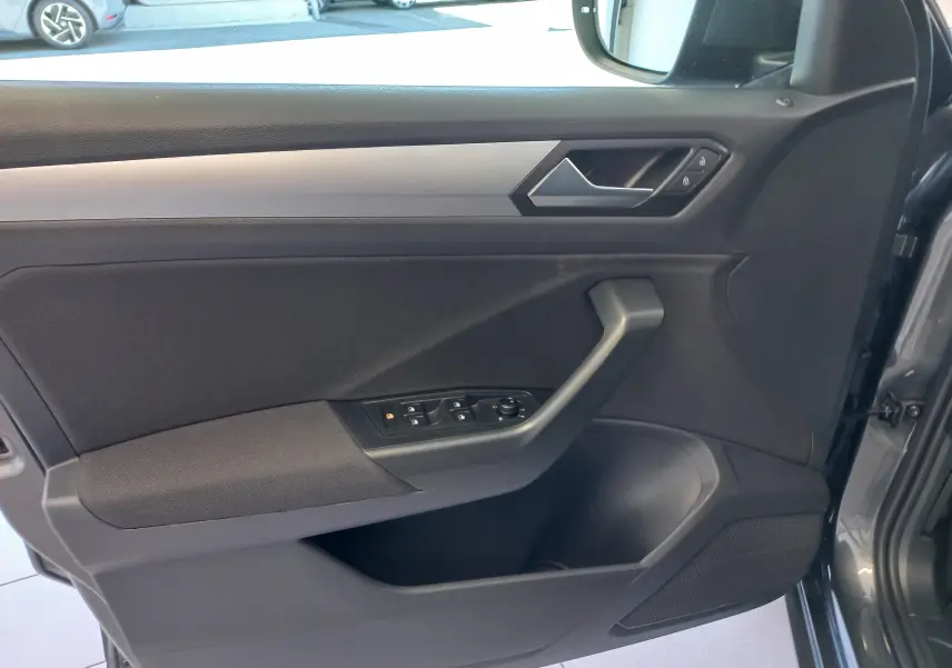 Vue intérieure côté gauche de la porte avant gris Indium du Volkswagen T-Roc 2025 avec commandes de vitres et miroir.