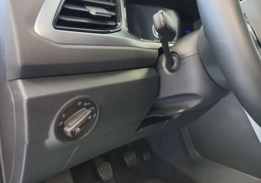 Détail intérieur côté gauche du tableau de bord du Volkswagen T-Roc 2025, avec commande des phares et pédales visibles.
