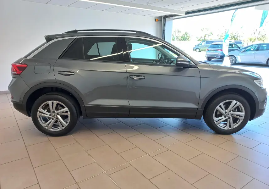 Vue de profil côté gauche d'un Volkswagen T-Roc 2025 gris Indium avec jantes alliage 17 pouces Valencia en intérieur showroom.