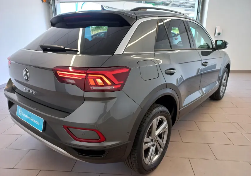 Vue 3/4 arrière droite du Volkswagen T-Roc 2025 gris Indium avec jantes alliage 17 pouces Valencia et feux arrière allumés.