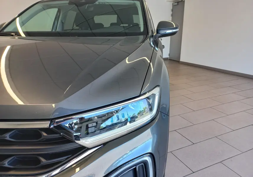 Vue rapprochée avant droite du Volkswagen T-Roc 2025 gris Indium, mettant en valeur le phare et la calandre.