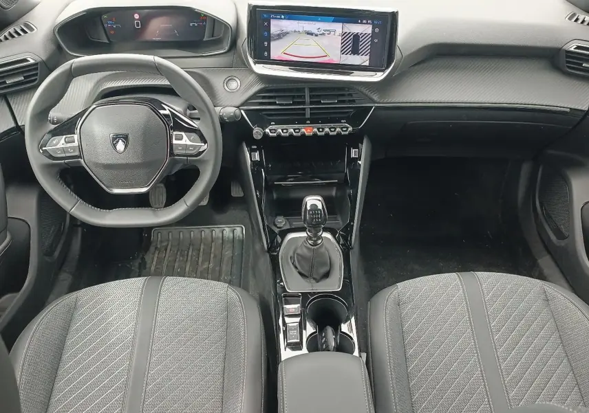 Vue intérieure frontale du poste de conduite du Peugeot 2008 1.2 100 allure, avec volant compact, écran tactile et levier de vitesses manuel.