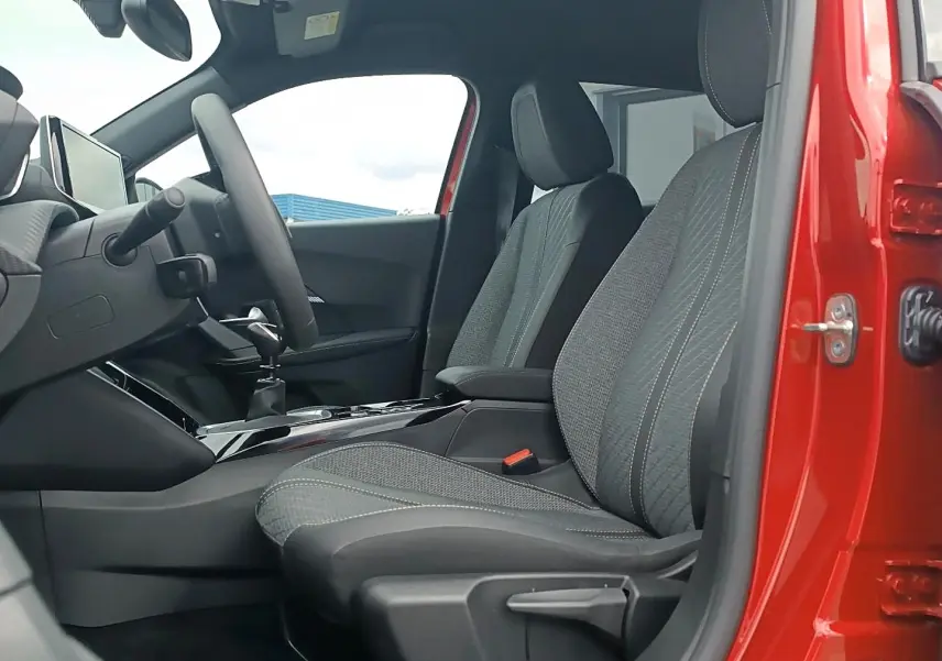 Vue intérieure côté conducteur du Peugeot 2008 rouge elixir, montrant les sièges en tissu gris et la console centrale.