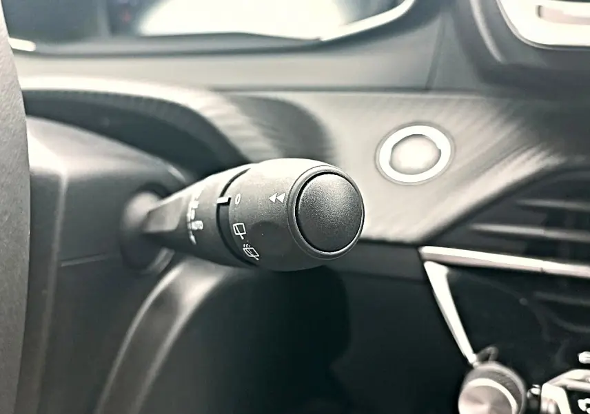 Gros plan sur la commande d’essuie-glace à gauche du volant dans l’habitacle noir du Peugeot 2008 Rouge Elixir.
