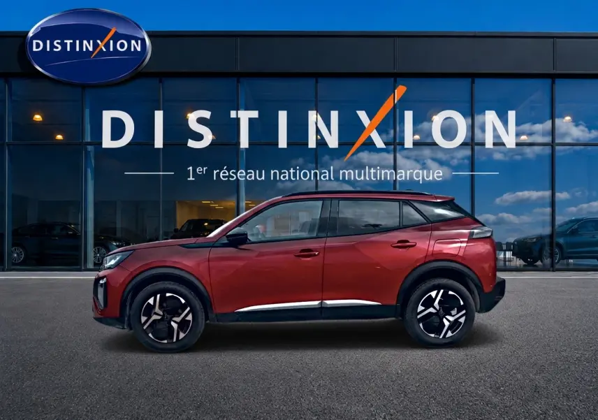 Profil latéral gauche d'un Peugeot 2008 rouge elixir avec jantes alu noires devant une vitrine Distinxion.