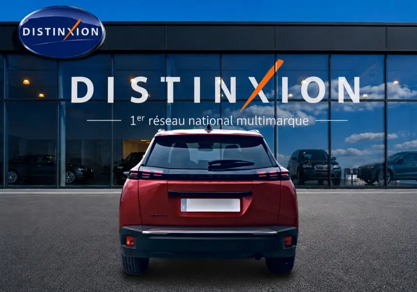 Vue arrière du Peugeot 2008 rouge Elixir 2025 avec feux LED distinctifs et becquet arrière, devant une vitrine Distinxion.
