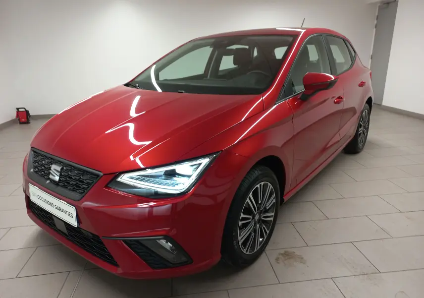 SEAT Ibiza 2025 rouge désir vue 3/4 avant droit, phares allumés et jantes alliage distinctives.