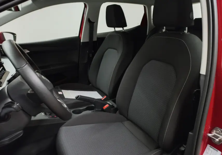Vue intérieure côté conducteur de la SEAT Ibiza 2025 rouge désir, sièges noirs avec coutures blanches et volant visible.
