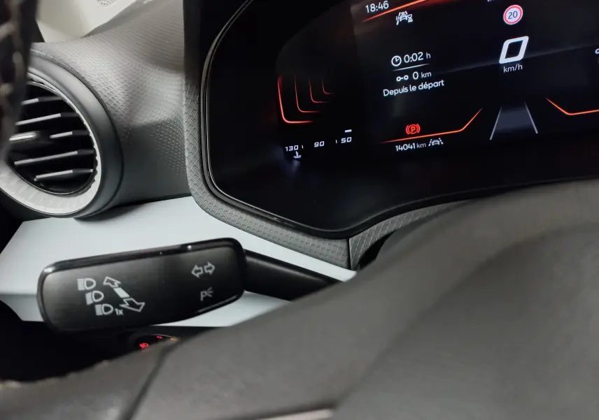 Vue intérieure rapprochée du tableau de bord et du commodo gauche de la SEAT Ibiza 2025, affichage numérique rouge et noir.