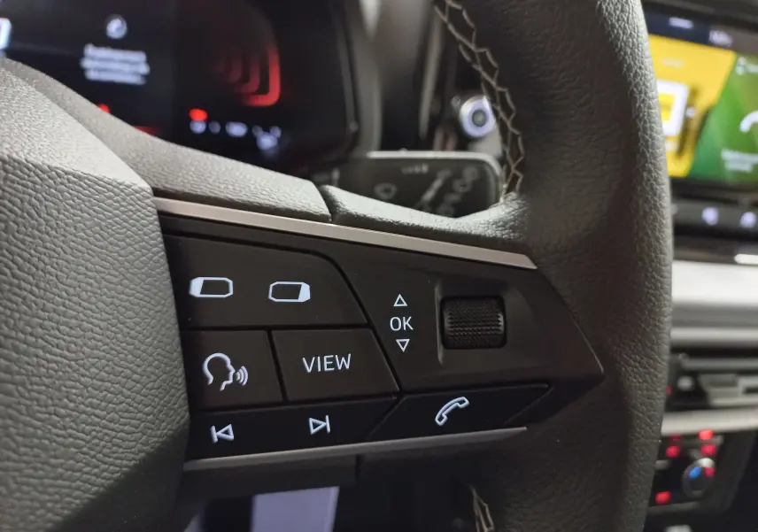 Gros plan sur les commandes au volant côté gauche du SEAT Ibiza 2025 Rouge Désir, avec boutons multifonctions et molette.