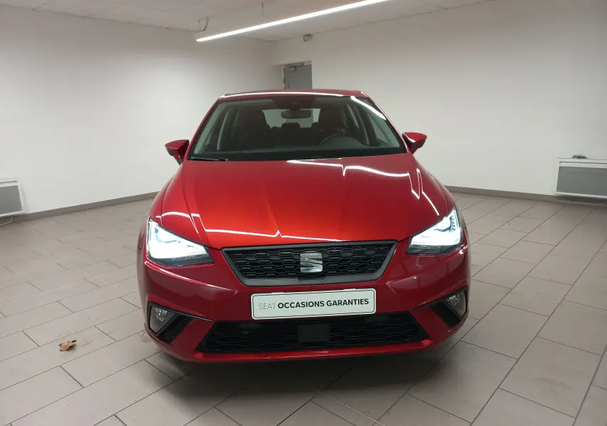 Vue frontale d'une SEAT Ibiza 2025 rouge désir avec phares allumés dans un showroom intérieur.