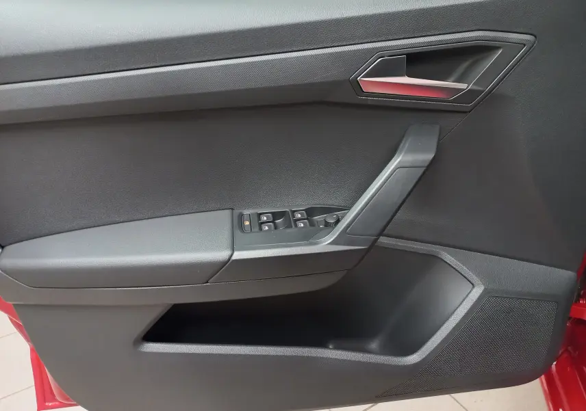 Vue intérieure côté gauche de la porte d’une SEAT Ibiza 2025 rouge désir, avec commandes de vitres et poignée intégrée.