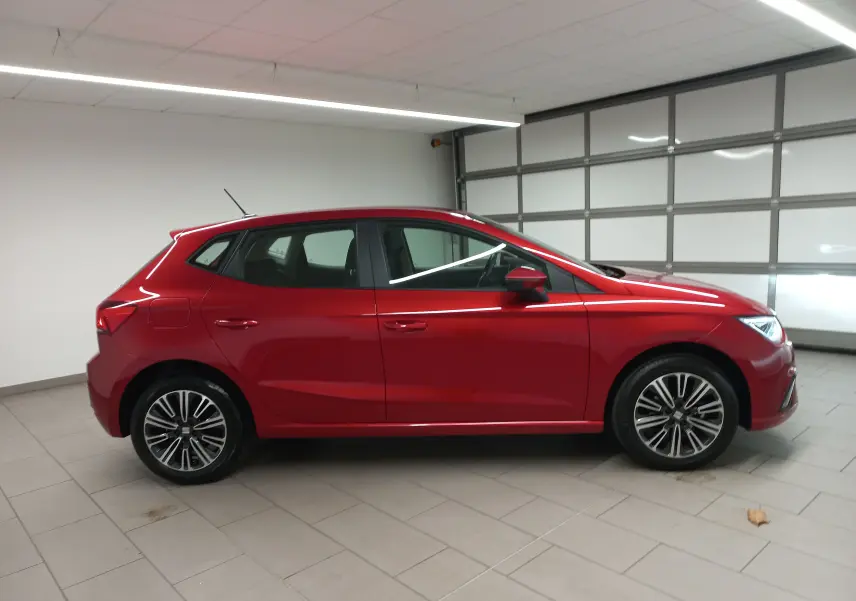 Vue de profil côté gauche d'une SEAT Ibiza 2025 Rouge Désir avec jantes alliage et antenne sur le toit dans un garage.
