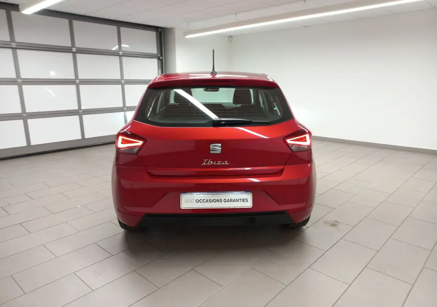 Vue arrière d'une SEAT Ibiza 2025 Rouge Désir, avec feux arrière allumés dans un garage lumineux.