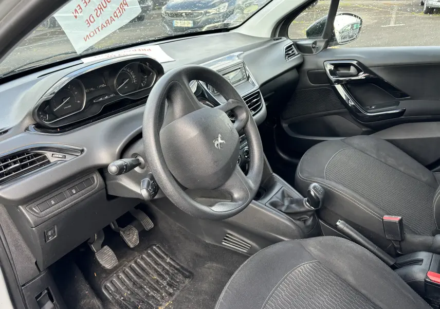 Intérieur noir de la Peugeot 208 2017, vue côté conducteur montrant volant, tableau de bord et levier de vitesse manuel.