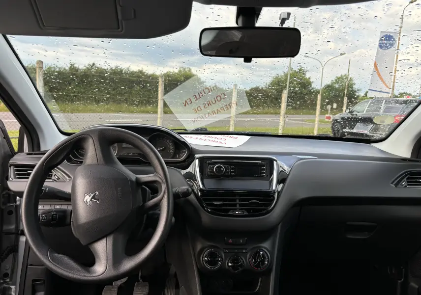Vue intérieure avant du tableau de bord noir de la Peugeot 208 gris argent 2017 avec volant et système audio central.