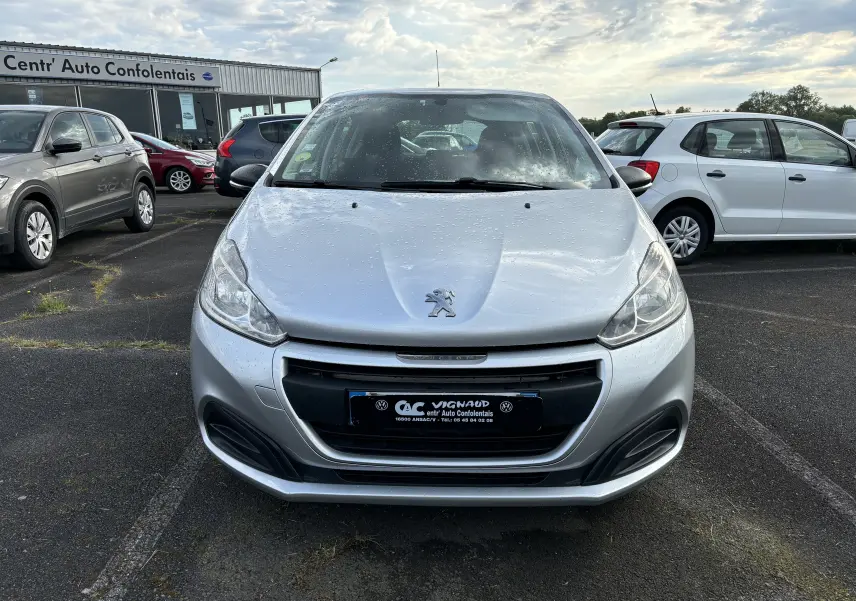 Vue frontale d'une Peugeot 208 gris argent 2017 avec gouttes d'eau sur le capot, stationnée sur un parking extérieur.