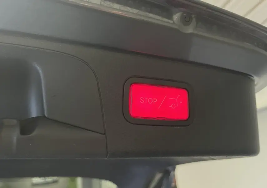 Bouton rouge d'arrêt électrique du hayon visible sous le coffre d'un Mercedes GLC gris, vue rapprochée intérieure.