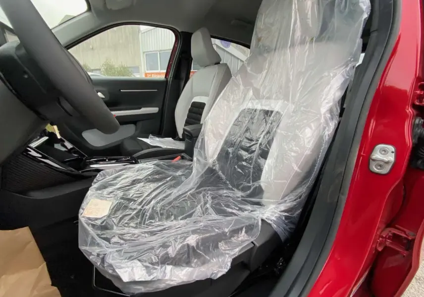 Vue intérieure côté conducteur du Citroën C3 Aircross rouge Elixir, sièges avant protégés par film plastique transparent.