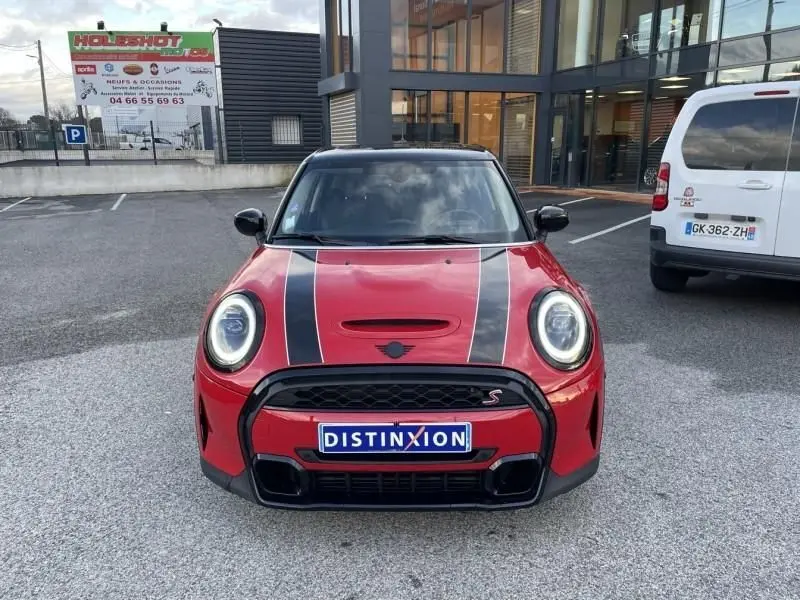 Vue frontale d'une MINI 5 portes rouge avec bandes noires sur le capot et calandre noire distinctive.