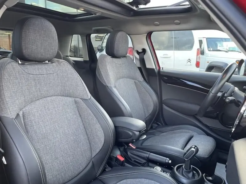 Vue intérieure côté avant droit de la MINI 5P Cooper D rouge, sièges tissu gris avec surpiqûres blanches et toit panoramique.