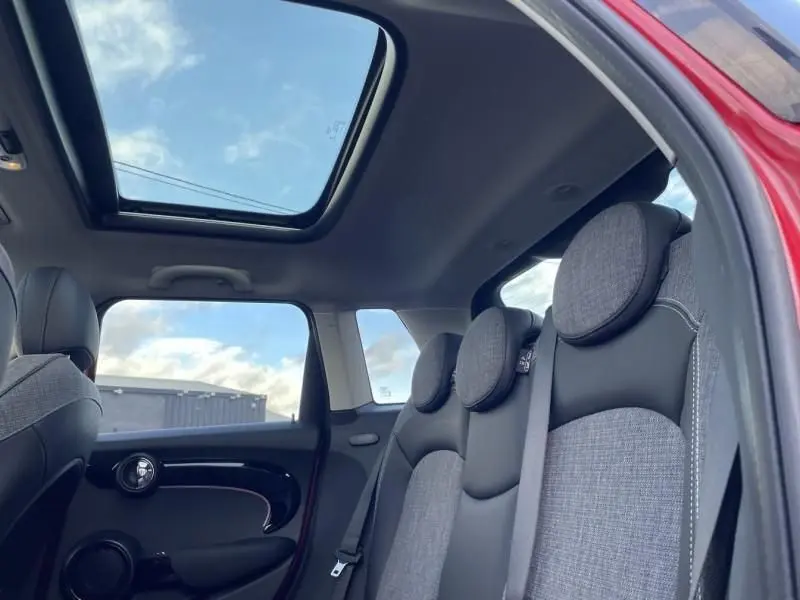 Vue intérieure arrière droite de la MINI 5P rouge 2021, montrant les sièges gris et le toit ouvrant panoramique.