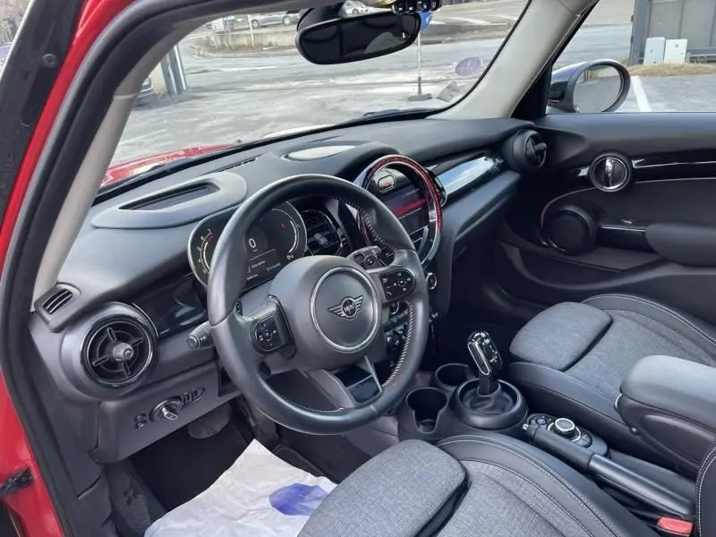 Vue intérieure côté conducteur de la MINI 5P Cooper D rouge, mettant en valeur le volant multifonction et la console centrale.