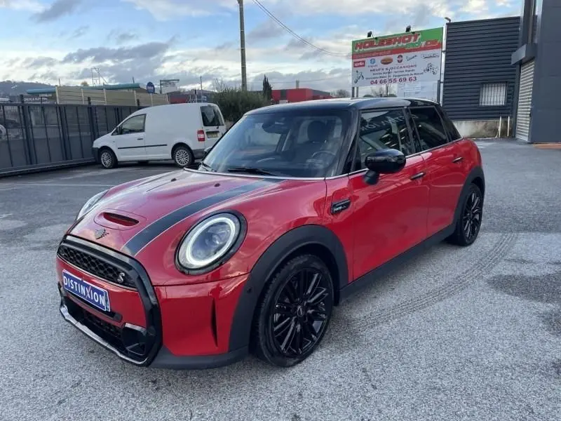 Vue 3/4 avant droite d'une MINI 5 portes rouge avec toit noir et bandes noires sur le capot, roues noires.