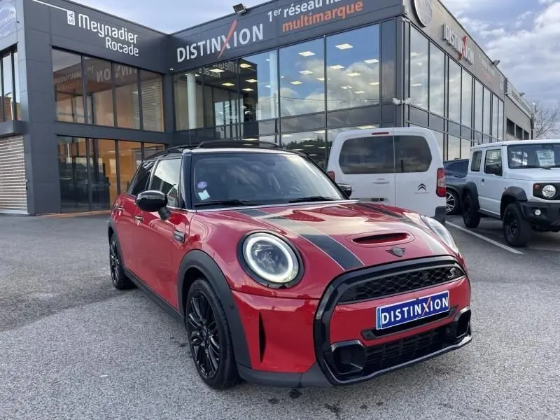 MINI 5 portes Cooper D rouge vue 3/4 avant droit avec bandes noires sur capot et jantes noires devant un showroom.