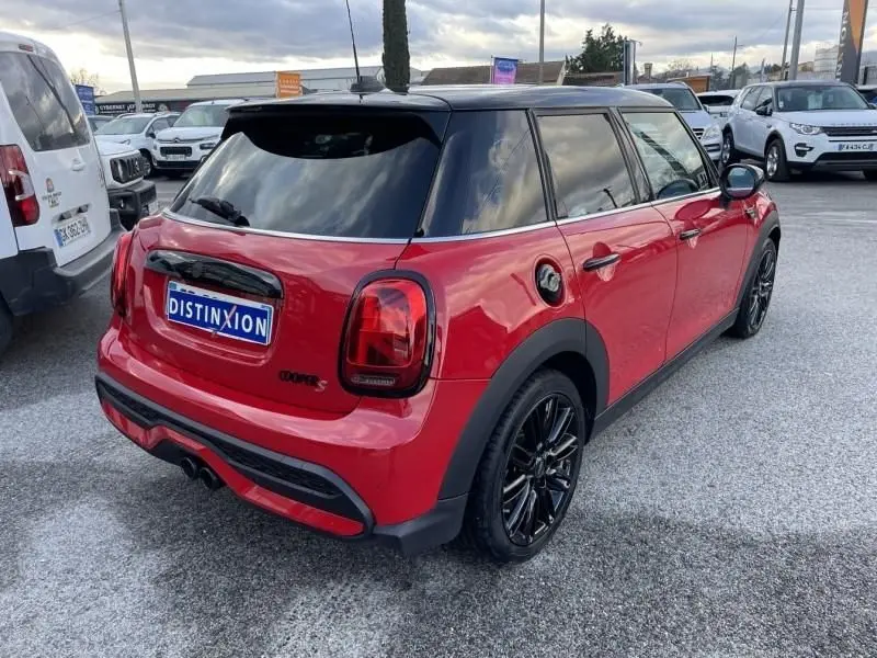 Vue 3/4 arrière droite d'une MINI 5 portes Cooper D rouge avec toit noir et jantes noires brillantes.