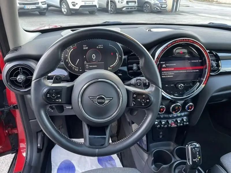 Vue intérieure centrée sur le volant et le tableau de bord numérique d'une MINI 5P rouge Edition Camden 2021.