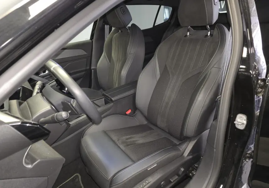 Vue intérieure côté conducteur de la Peugeot 408 GT 1.2i Hybrid 2024, sièges noirs en cuir et tissu avec surpiqûres grises.