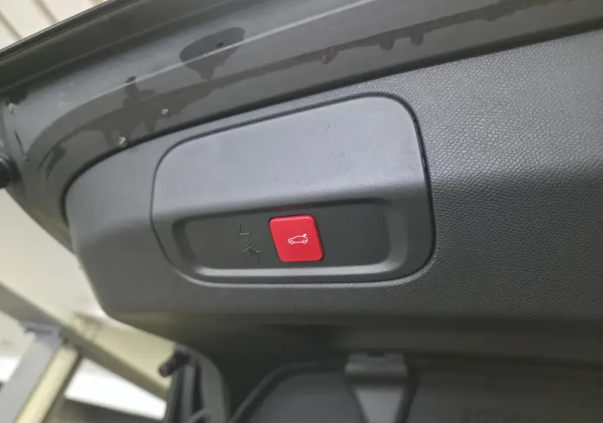Gros plan sur le bouton rouge d'ouverture électrique du hayon du coffre d'une Peugeot 408 noire.