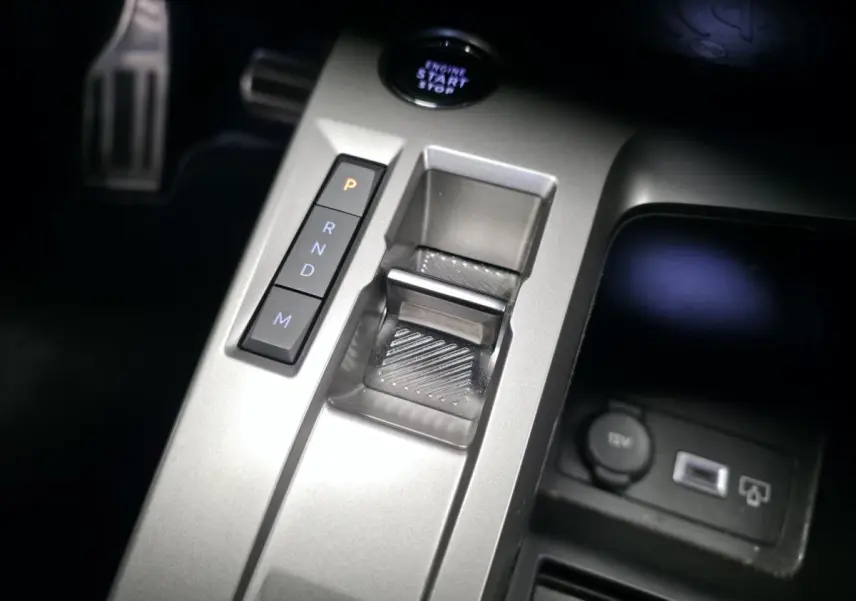 Gros plan sur la console centrale argentée de la Peugeot 408 Hybrid 2024 avec sélecteur de boîte auto et bouton start/stop.