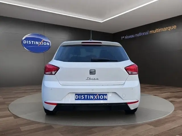 Vue arrière d'une SEAT Ibiza blanche 2023 avec vitres arrière surteintées, sur fond gris en showroom.