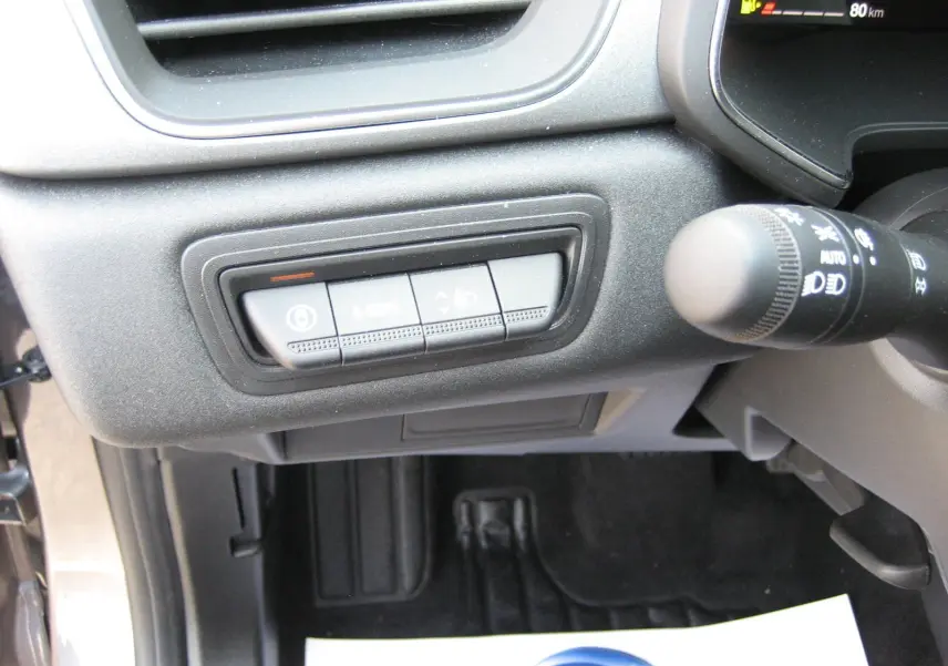 Gros plan sur les commandes sous le tableau de bord côté gauche du Renault Symbioz gris Rafale, avec levier de clignotant visible.