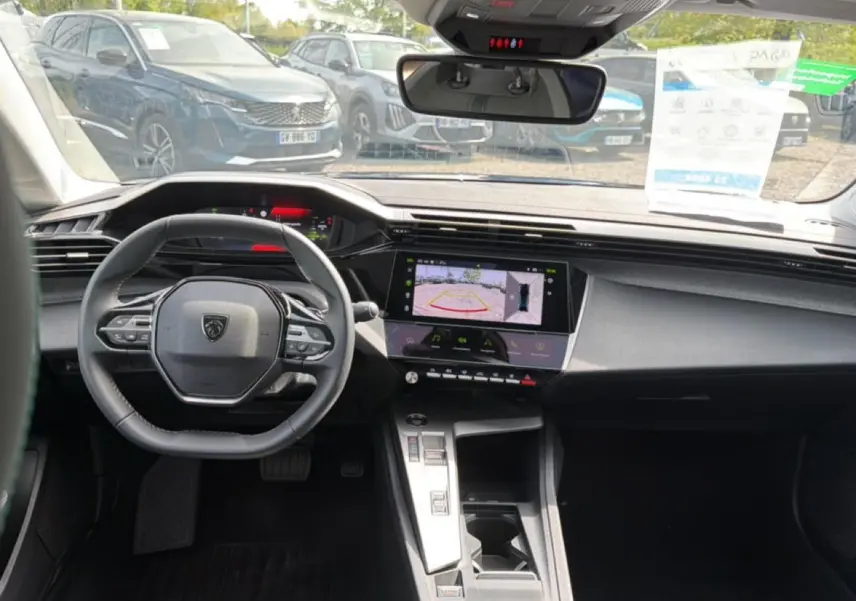 Vue intérieure avant de la Peugeot 408 Hybrid 136 allure 2024, tableau de bord noir avec écran tactile et volant cuir.
