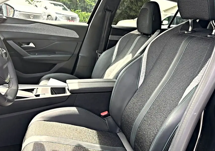 Vue intérieure côté gauche de la Peugeot 408 Hybrid 136 allure 2024, sièges tissu et cuir noir avec accoudoir central.