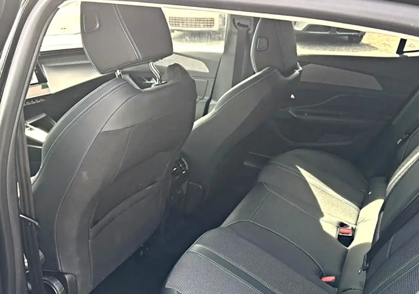 Vue intérieure arrière droite de la Peugeot 408 Hybrid 136 allure e-dcs6 noire, montrant les sièges et les finitions tissu et cuir.