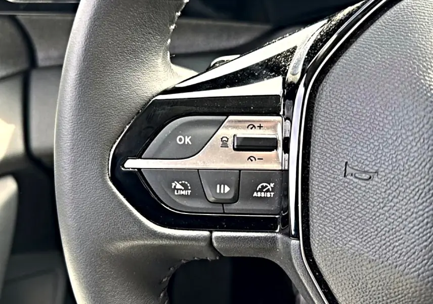 Gros plan sur le côté gauche du volant cuir noir du Peugeot 408 Hybrid 136 allure avec commandes de régulateur et assistant.