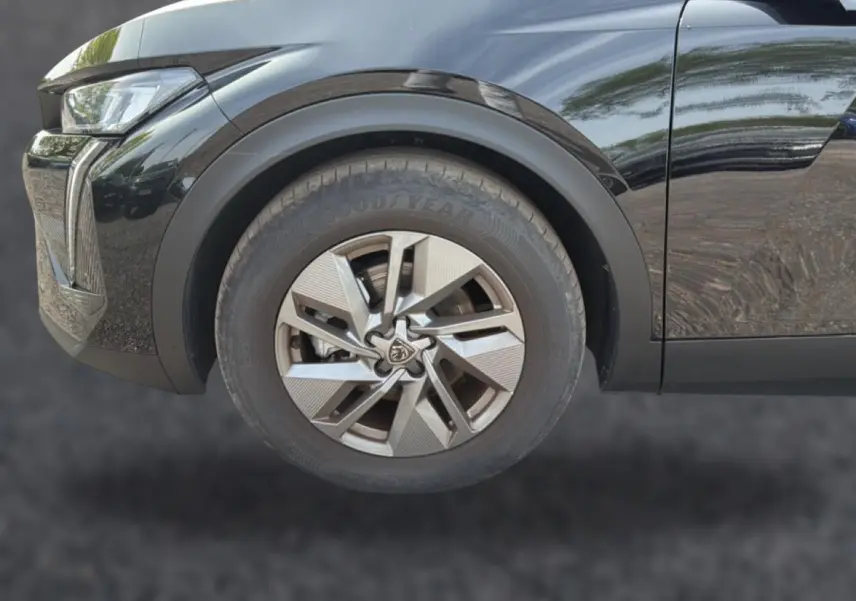Gros plan sur la roue avant gauche noire d’une Peugeot 408 Hybrid 136 allure 2024 avec jante alu et phare LED partiel.