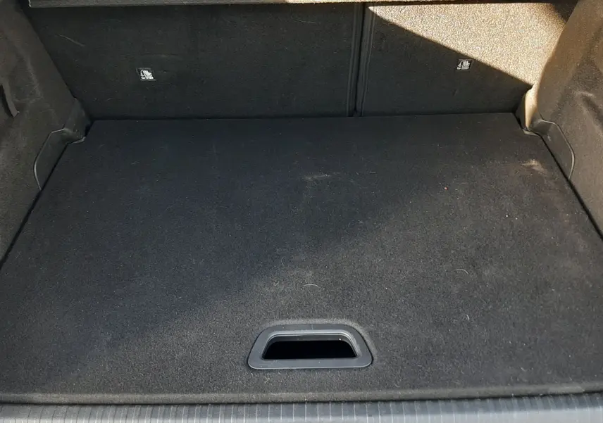 Vue plongeante sur le coffre vide de la Citroën C4 gris 2023, montrant la moquette noire et la poignée d'accès au rangement inférieur.