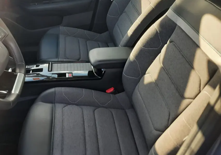 Vue intérieure côté avant droit de la Citroën C4 gris 2023, sièges tissu gris avec surpiqûres et accoudoir central noir.
