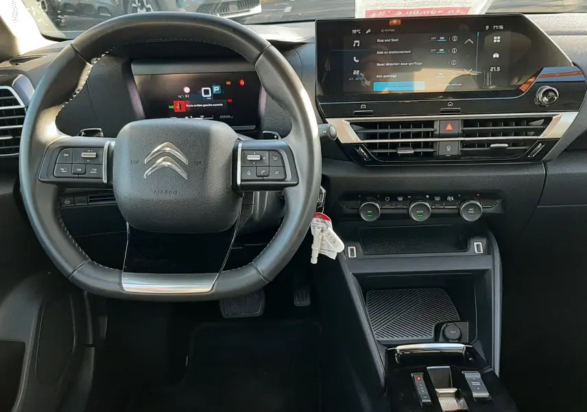 Vue intérieure frontale du poste de conduite d'une Citroën C4 gris 2023, avec volant multifonctions et écran tactile central.