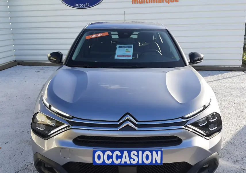Vue avant d'une Citroën C4 gris métallisé 2023 avec plaque "OCCASION" et autocollant "DIESEL" sur le pare-brise.