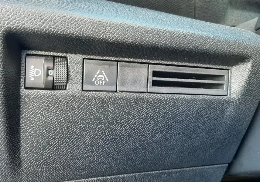 Détail intérieur côté gauche du tableau de bord gris d'une Citroën C4 2023 avec commandes de réglage des phares et d'alerte de franchissement de ligne.